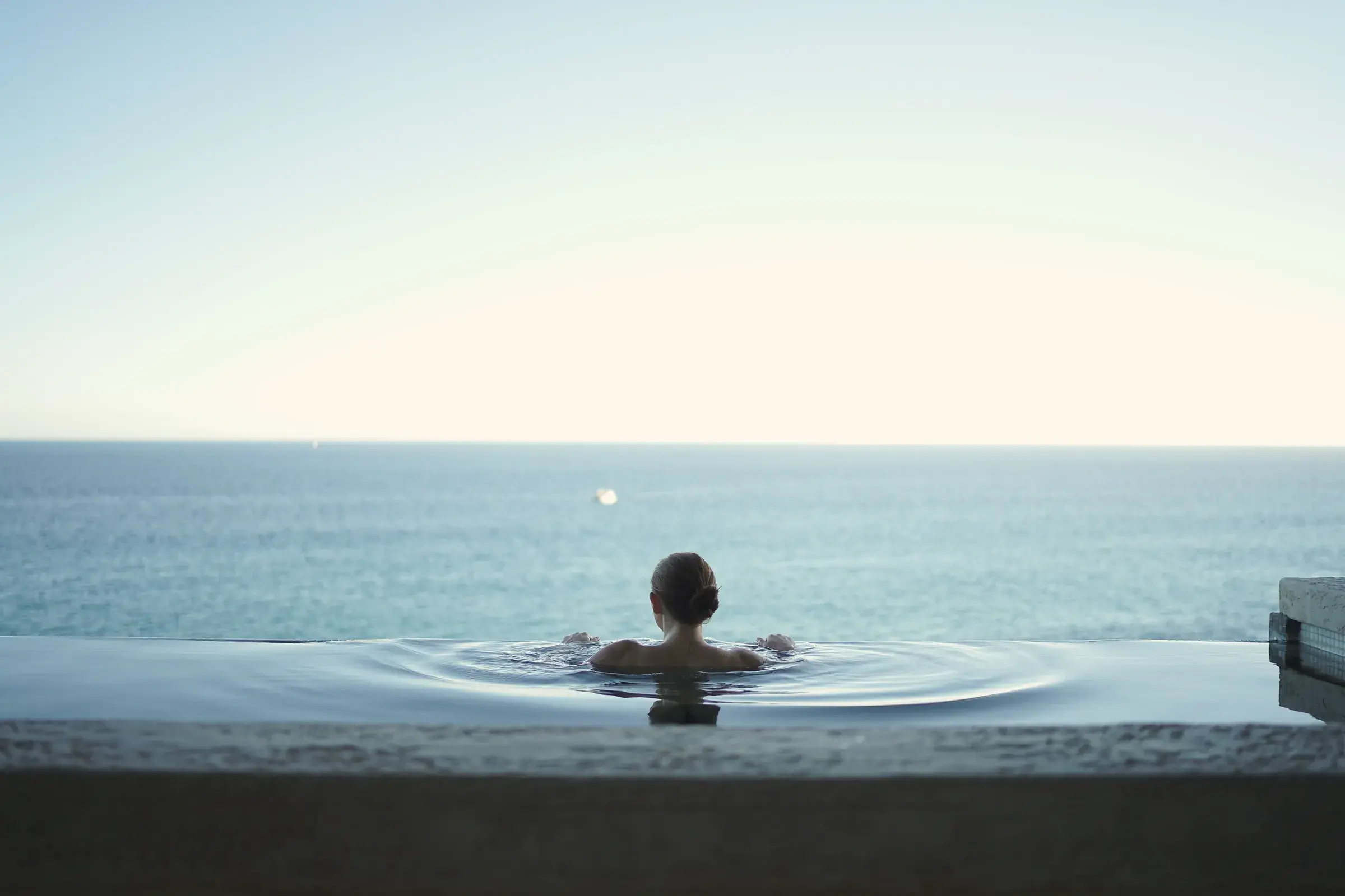 Swimmer seen from behind in an infinity pool facing the open sea