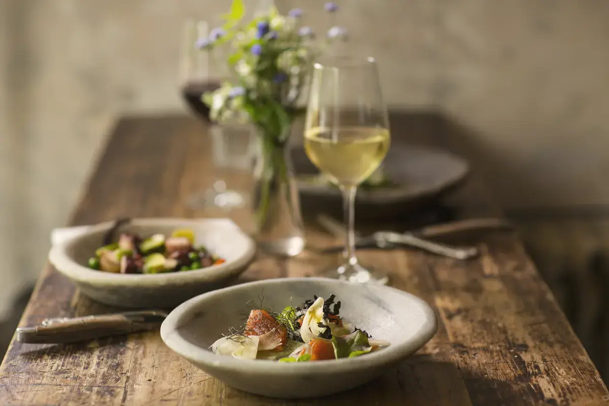 Two plated dishes and glasses of wine on a rustic wooden table