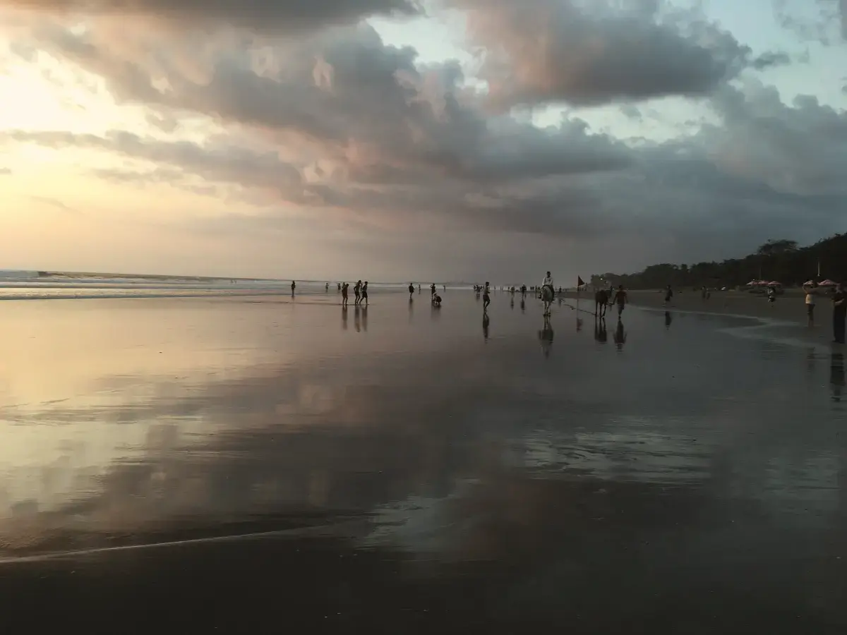 Seminyak beach at dusk, wet sand reflecting a cloudy sunset sky