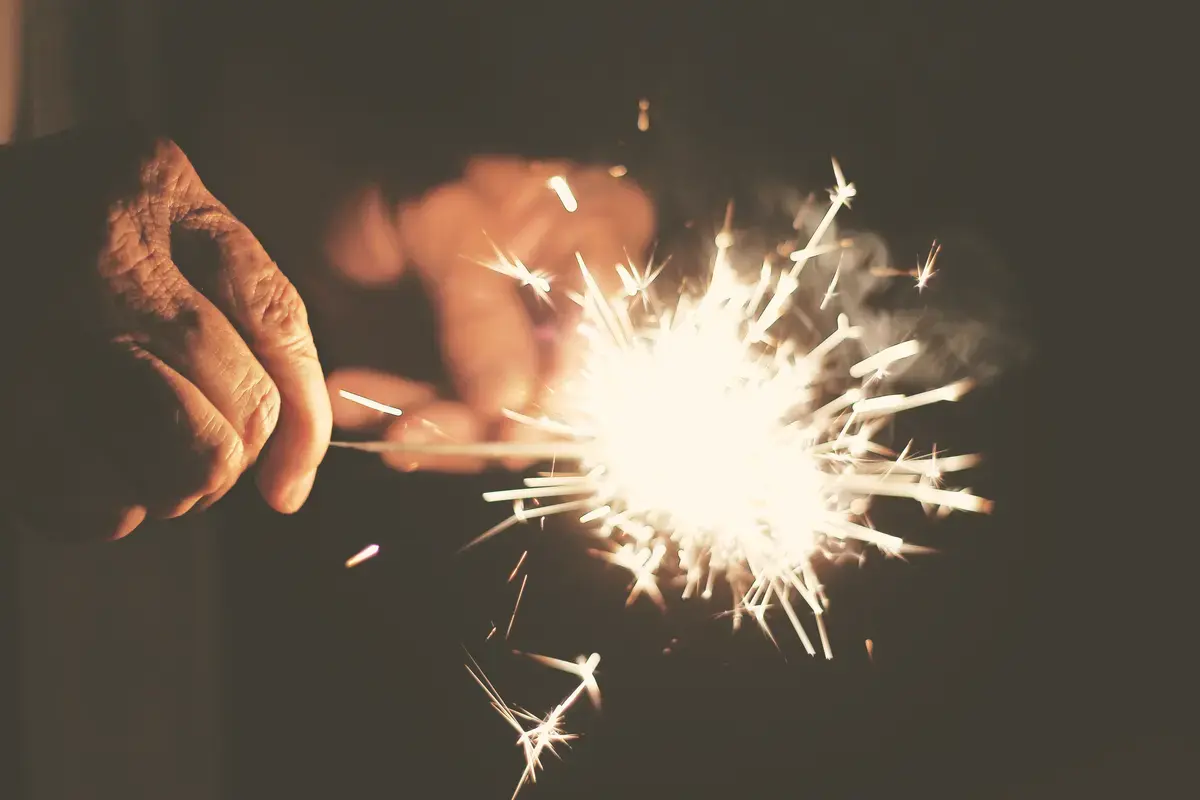 A lit sparkler held between fingers against a dark background