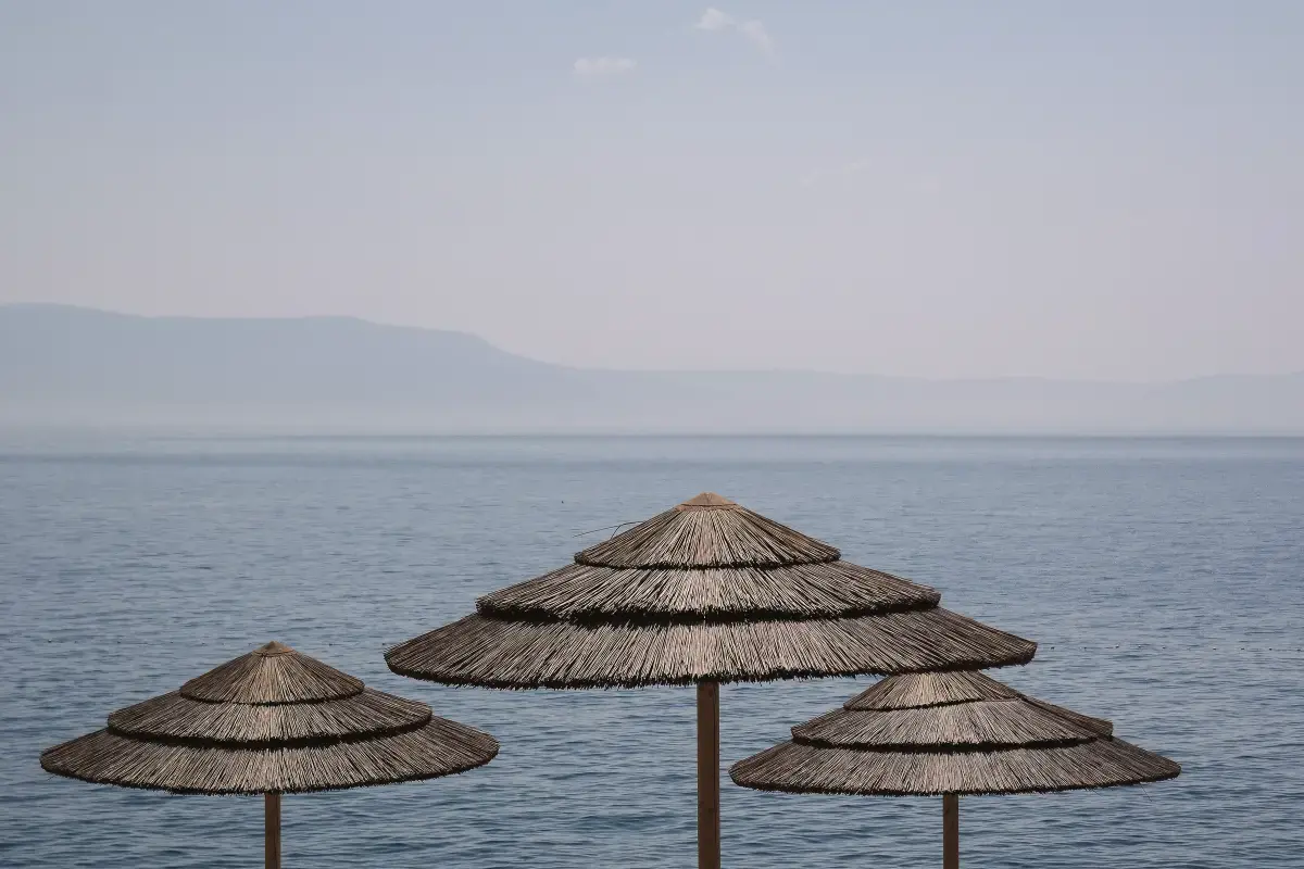 Trois parasols en paille face à une mer calme et brumeuse