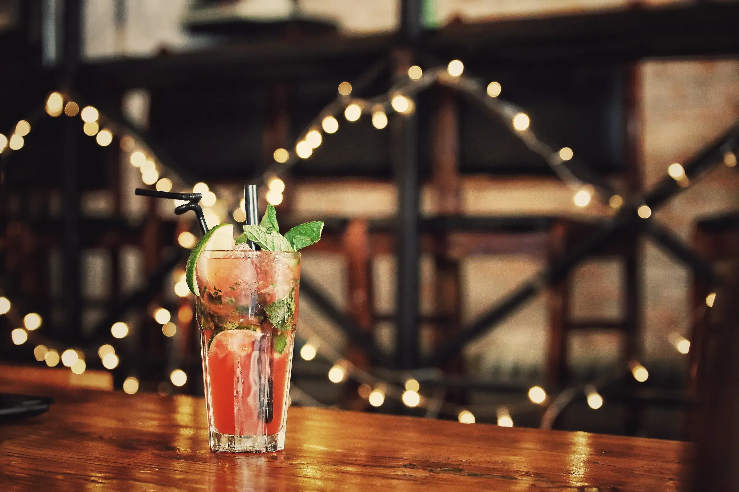 Cocktail with mint and lime on a bar counter, string lights in the background