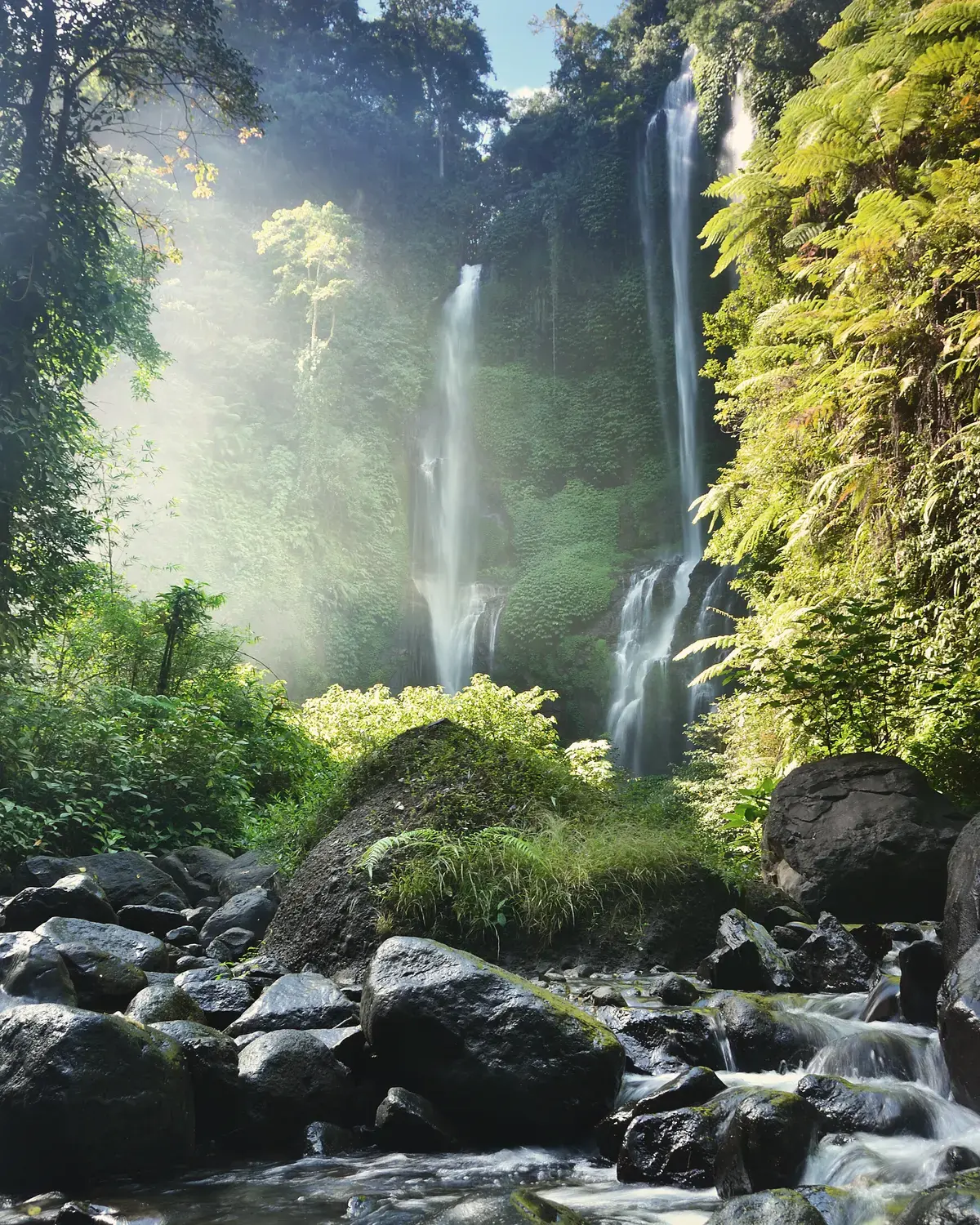 Sekumpul waterfalls dropping through dense jungle onto a rocky stream, north Bali