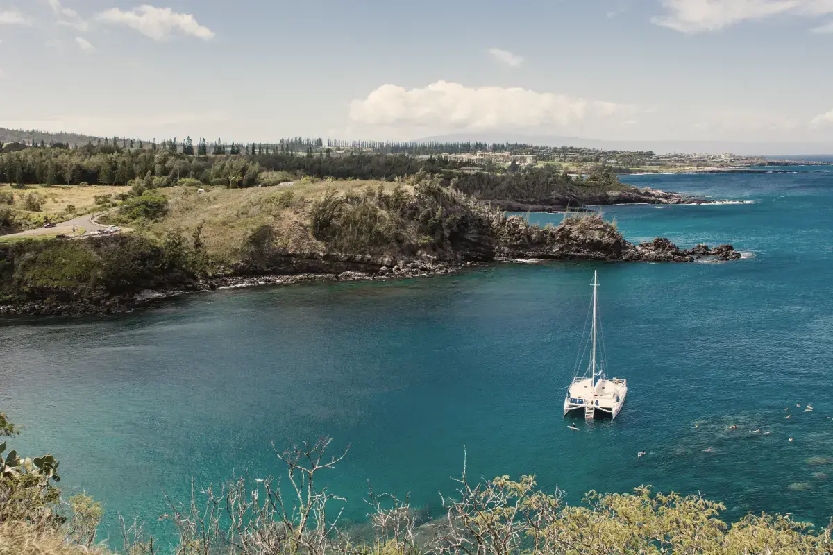 Catamaran at anchor in a turquoise bay below green headlands, Maui