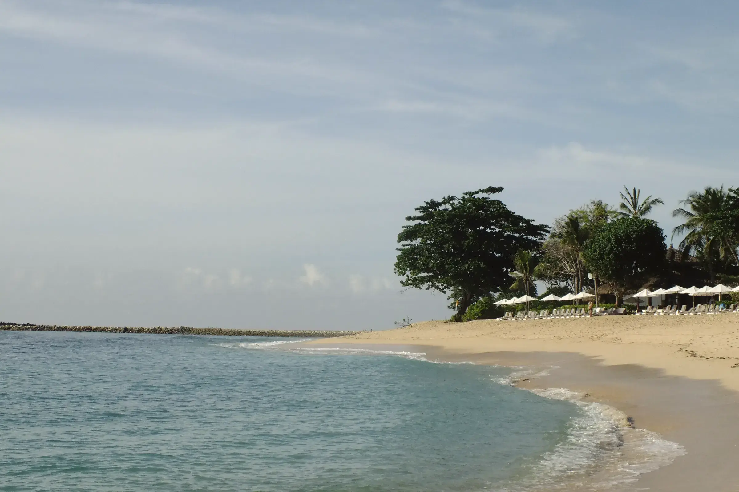 Calm turquoise water lapping a curve of pale sand fringed by trees, Nusa Dua